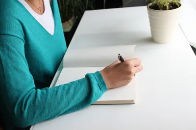 A woman writing in a notebook at a minimalist white desk indoors, emphasizing productivity.