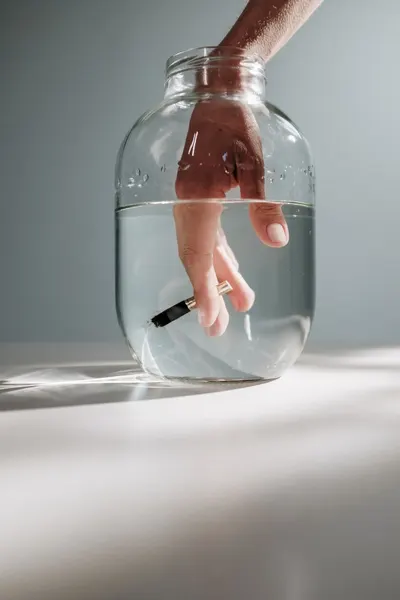 Artistic shot of a hand submerged in a jar of water, creating an abstract and conceptual effect with lighting.