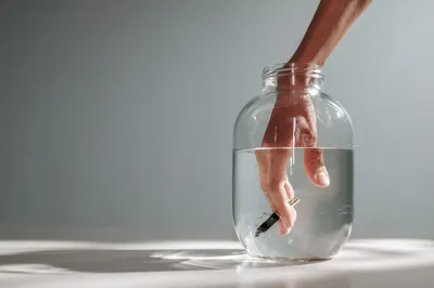 Close-up of a hand submerged in a clear jar filled with water, creating a visual play of distortion and transparency.