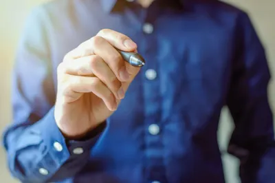Close-up of a person holding a pen, ready to write, with blurred background.