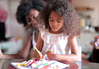 Creative girl with curly hair intensely focused on drawing with markers at home.