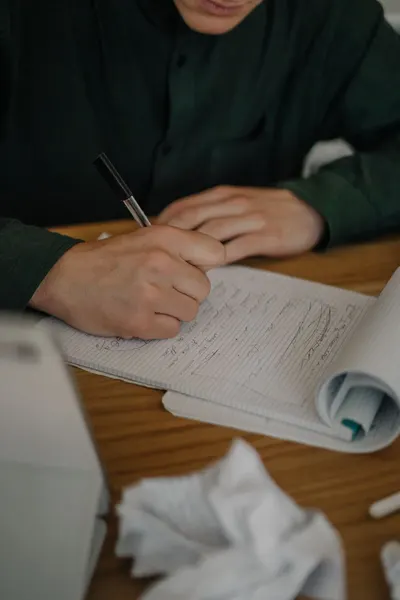 Detailed close-up of a person writing notes on paper at a wooden desk, with focus on the hands.