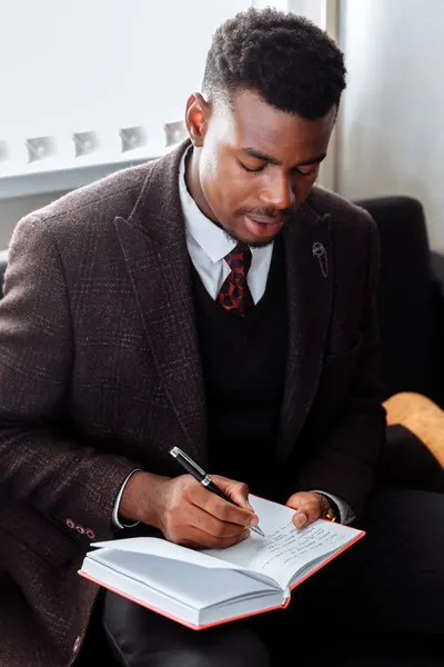 Businessman in office attire writing notes in a journal with focus and precision.