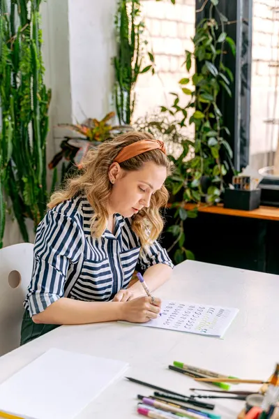 A young woman engaged in creative hand lettering practice in a cozy art studio.