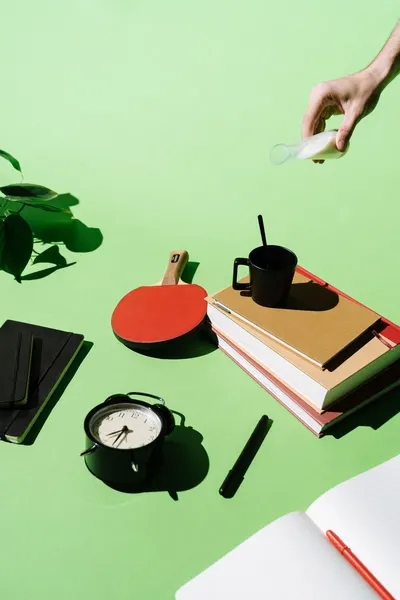 Artistic composition featuring books, clock, ping pong paddle, and coffee on a bright green background.