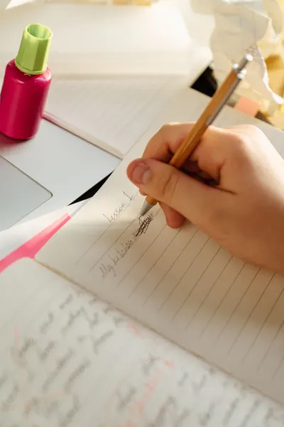 A person writing in a journal using a ballpen, with sunlight streaming over crumpled papers.