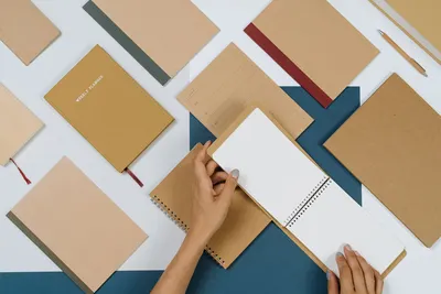 Hands flipping a spiral notepad amid brown stationery in a flat lay setup.