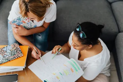 Two women collaborating on study notes in a cozy indoor setting, fostering teamwork.