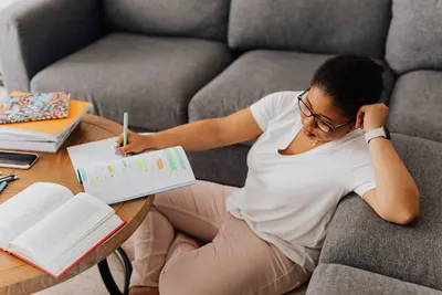 Tired African American woman studying with notebooks at home, resting on sofa.