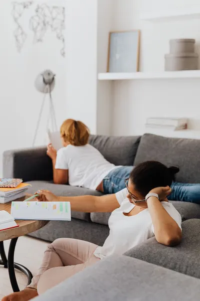 Two young adults studying in a cozy modern living room, surrounded by open books and comfortable furniture.