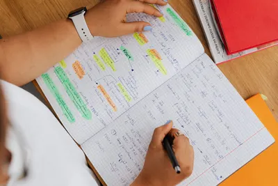 Close-up of hands writing in a notebook, highlighting study notes with pens and colorful markers.