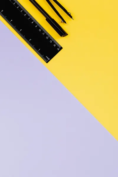 Flat lay of school supplies including pen, pencil, and ruler on a vibrant yellow and purple background.