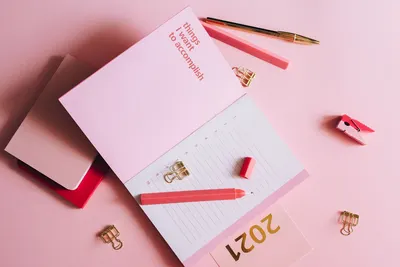 Organized workspace with pink planner, pen, and clips on pastel background.
