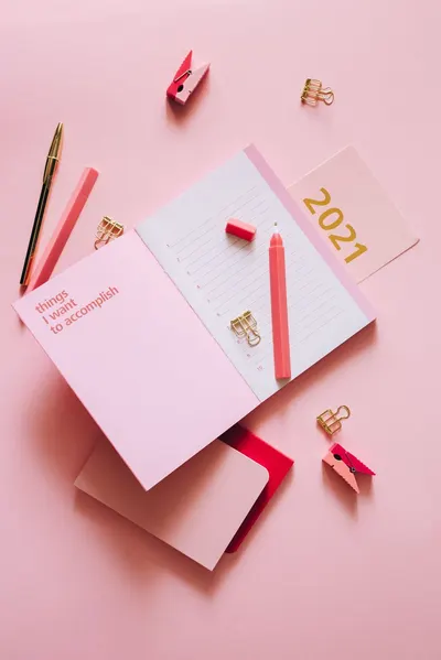 A stylish flat lay of a pink planner, 2021 notebook, and accessories on a pink surface.