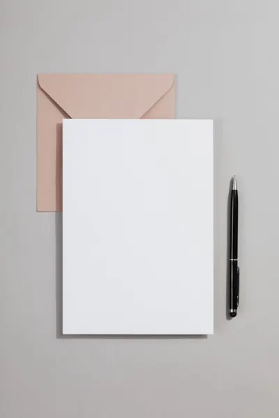 Minimalist stationery layout featuring a blank card, envelope, and pen on a grey background.