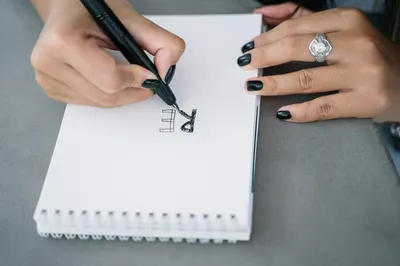Focused close-up of hand sketching letters on a notepad, showcasing creativity and style.