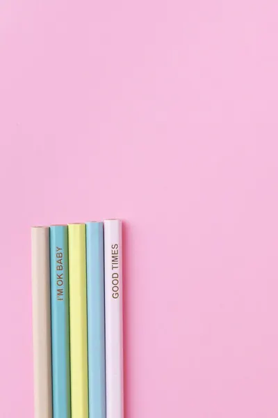 Vertical shot of pastel colored pencils with fun phrases on a pink surface.
