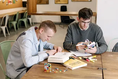 Two young men studying with books and highlighters in a library setting, focused and engaged.