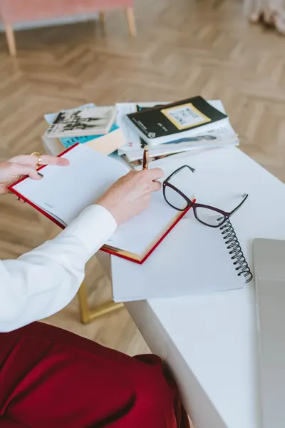Close-up of a person writing in a notebook with glasses and books nearby. Perfect for work or study themes.