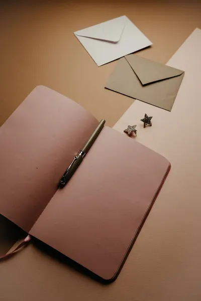A flat lay of an open notebook with a pen and envelopes on a neutral background.