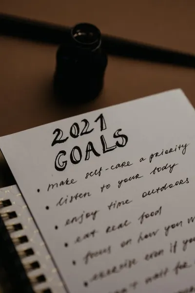 Close-up of a 2021 goals list on paper with ink bottle and fountain pen in a cozy setting.