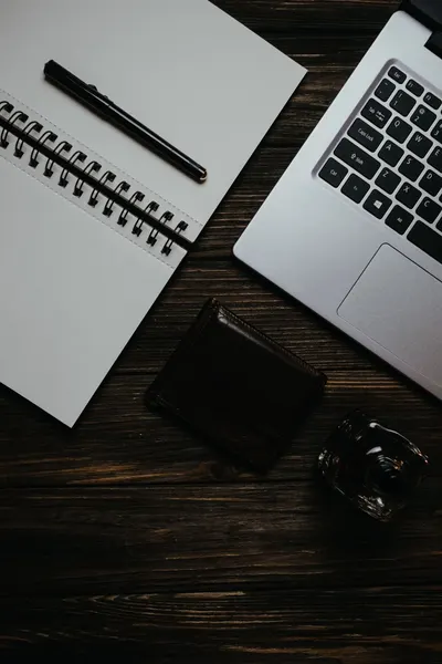 Stylish top view of a desk workspace featuring a laptop, notebook, pen, and wallet on a wooden surface.