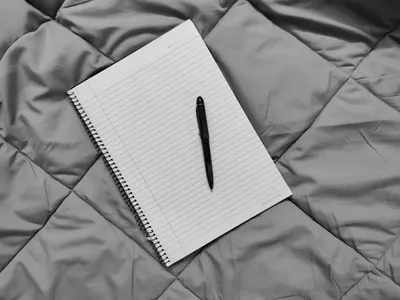 A spiral notebook with pen on a quilted gray comforter, perfect for cozy writing moments.