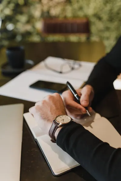 A close-up of a person writing with a pen, highlighting a luxury wristwatch.