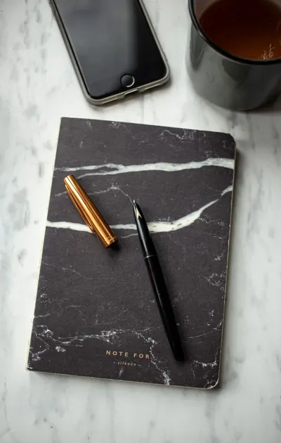Marble notebook and pen on a desk with coffee and smartphone, perfect for a creative workspace.