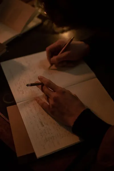 A person writing in a notebook while holding a cigarette in a dimly lit room, evoking a contemplative mood.