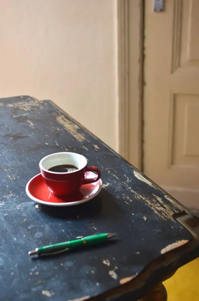 High angle of red ceramic cup of tasty hot fresh coffee placed on shabby wooden table near pen at home