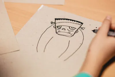 Close-up of a child drawing a cartoon character on paper with a black pen.