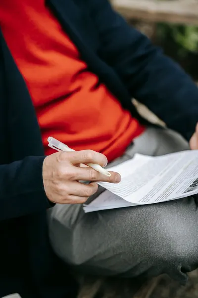 A focused individual reviewing documents outdoors, pen in hand, wearing vibrant clothing.