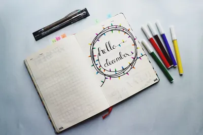 Open planner with 'Hello December' design surrounded by colorful markers, perfect for planning inspiration.