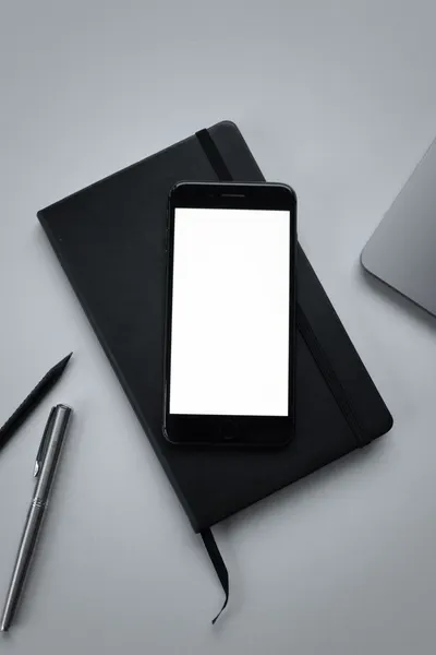 Flat lay of smartphone on a notebook with a pen and laptop, perfect for productivity themes.