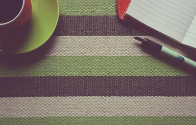 A stylish workspace setup featuring a coffee cup, notebook, and pen on a striped placemat.