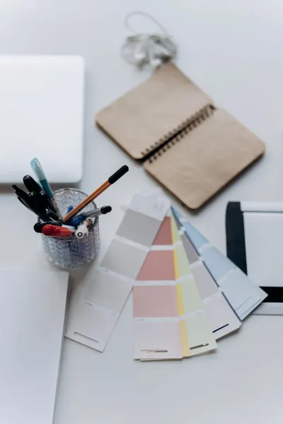 Organized workspace featuring color swatches, notebook, laptop, and stationery for design projects.