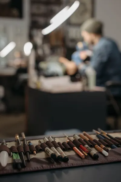 Close-up of tattoo tools with blurred artist in a modern studio setting.