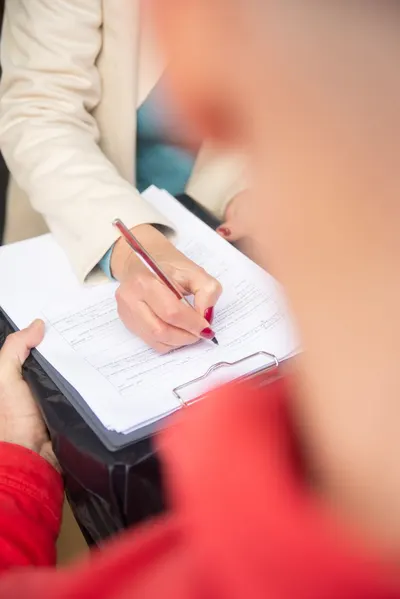 Close-up of a woman writing on a clipboard outdoors, hands holding a pen.
