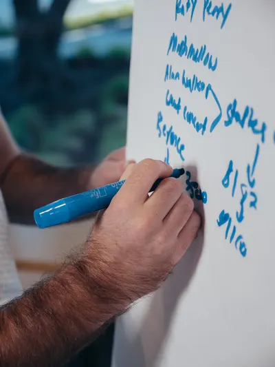 A man brainstorming ideas on a whiteboard using a blue marker indoors.