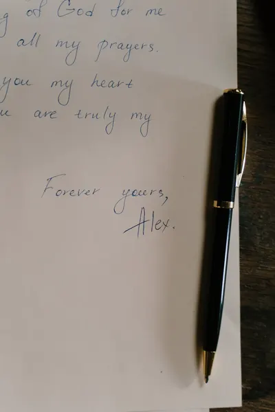 A close-up of a handwritten letter with a black pen on a wooden desk, conveying personal sentiments.