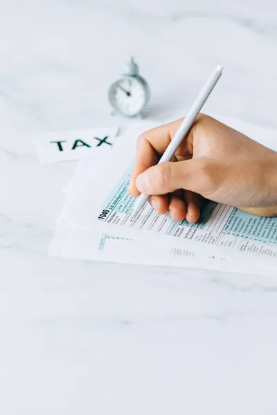 Hand completing tax forms with a pen, symbolizing financial deadline and time urgency.