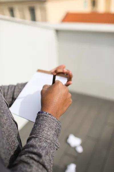 Close-up of a man writing on a notepad outdoors, focusing on hands and paper.