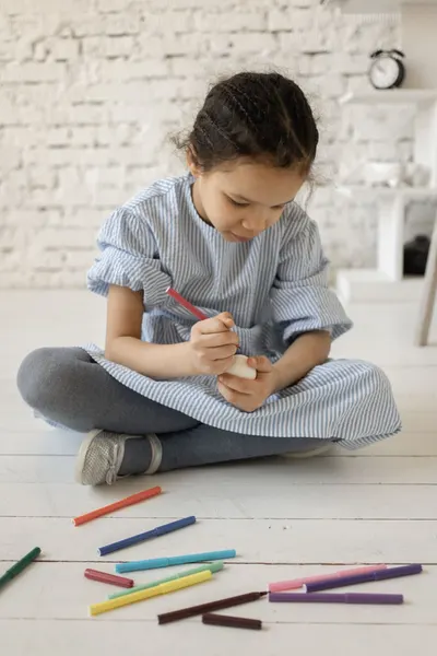Young girl sitting on the floor drawing with colorful pencils in a cozy room.