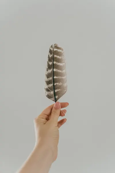 A delicate hand gently holding a feather against a soft white background, symbolizing grace and lightness.