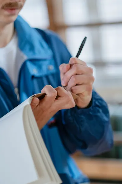 Close-up of a person writing notes in a blue jacket indoors.