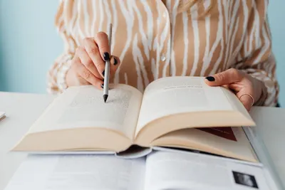 A person with a pen pointing at text in an open book, focusing on study or research.