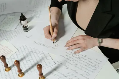 A woman practices elegant calligraphy with ink and paper, showcasing artistic hand lettering.