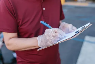 A person wearing gloves writes on a clipboard outdoors in casual attire.