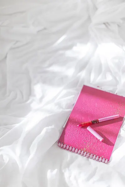 Pink notepad with pen on soft white fabric, artistic and minimalist setup.